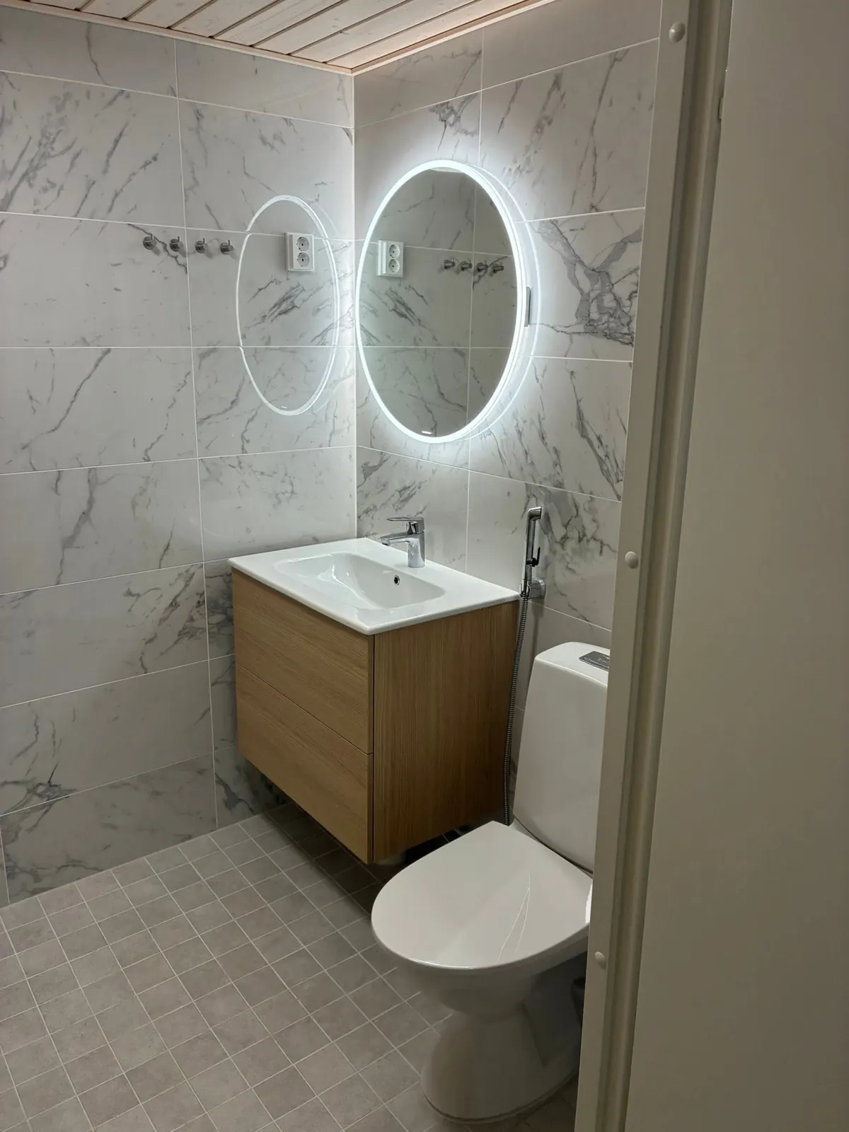 WC, jossa valaistu pyöreä peili ja puinen allaskaappi
